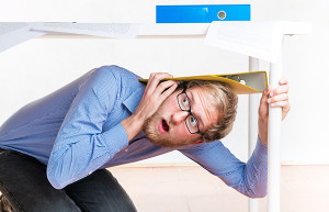 Employee hiding under a desk during an earthquake